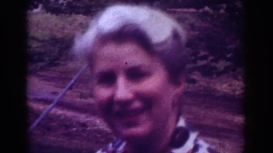 1962 Raleigh 8mm frame of an older woman smiling toward the camera in an outdoor garden-like setting.