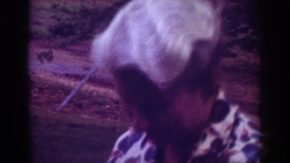 Older woman with short white hair in a patterned blouse stands outdoors in Raleigh home-movie footage from 1962.