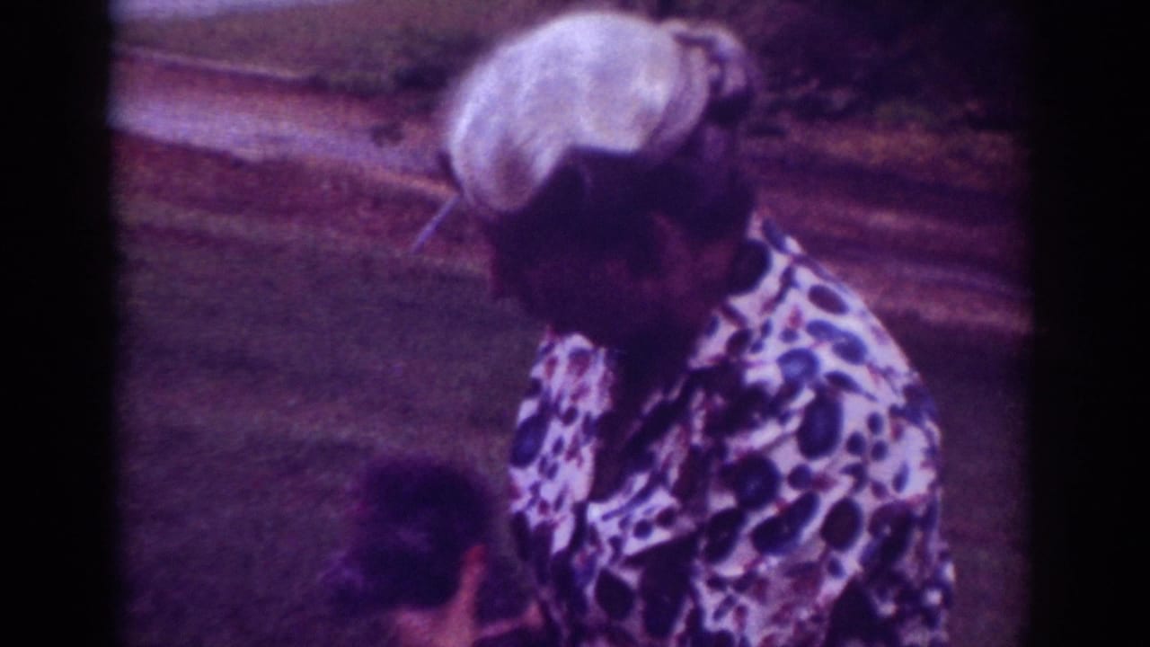 In Raleigh, 1962 home-movie footage, a woman in a patterned blouse bends toward a small dark dog near a grassy roadside.