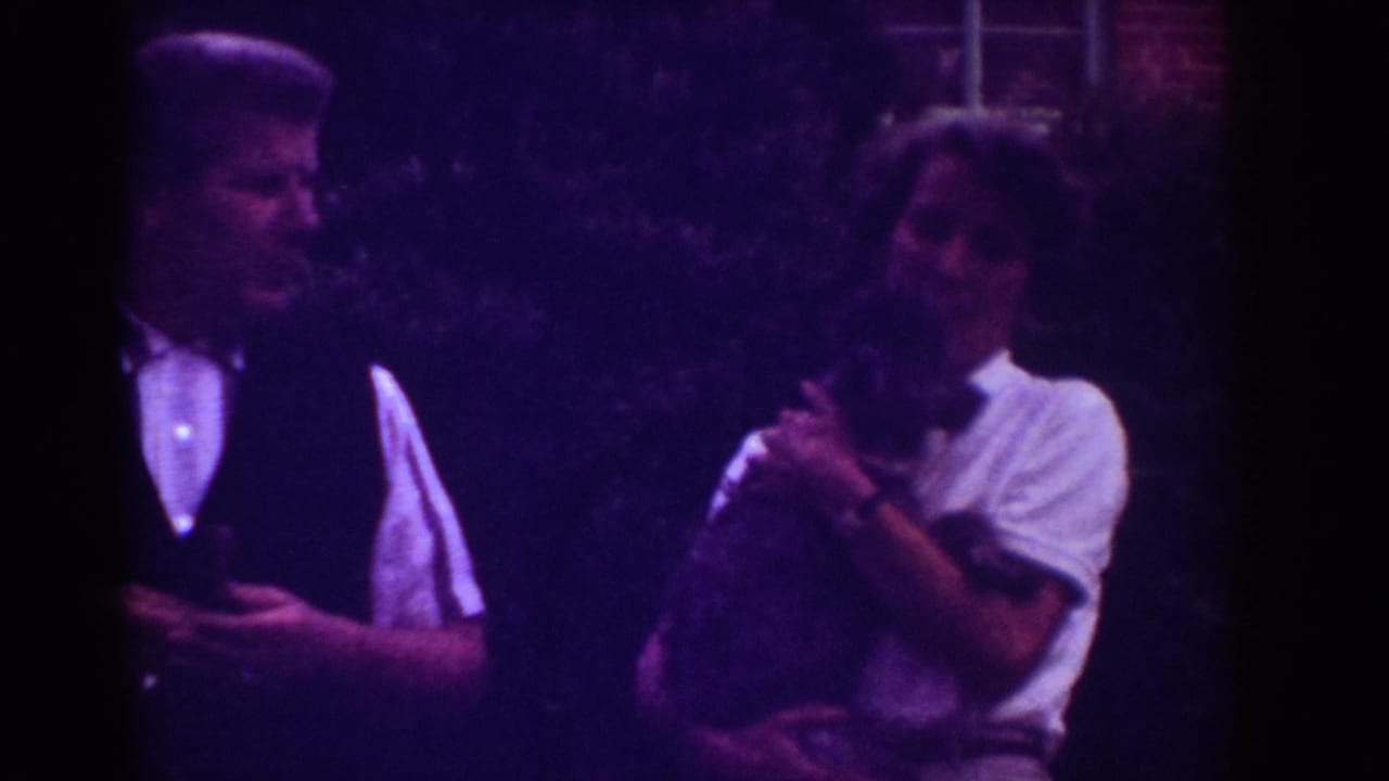 In Raleigh 1962 home-movie footage, two adults appear outdoors at night, with one formally dressed man beside another person holding a small animal.