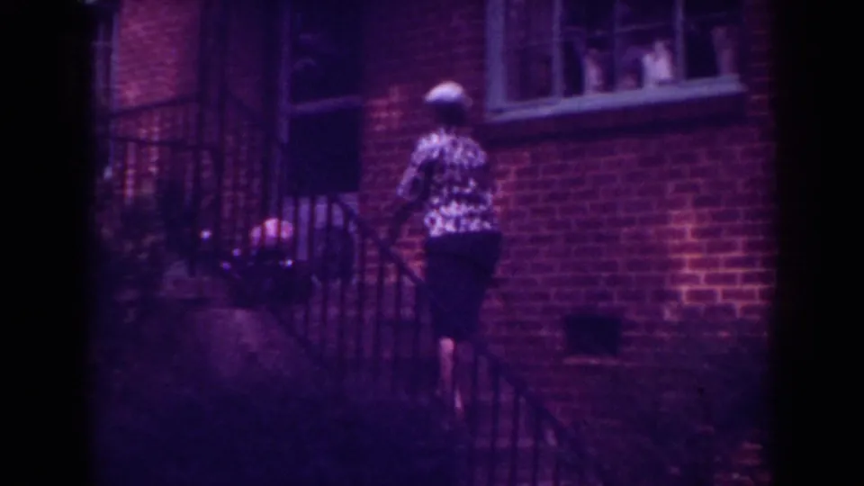 In the Raleigh 1962 footage, a woman in a patterned blouse walks up exterior steps along a brick residential building.