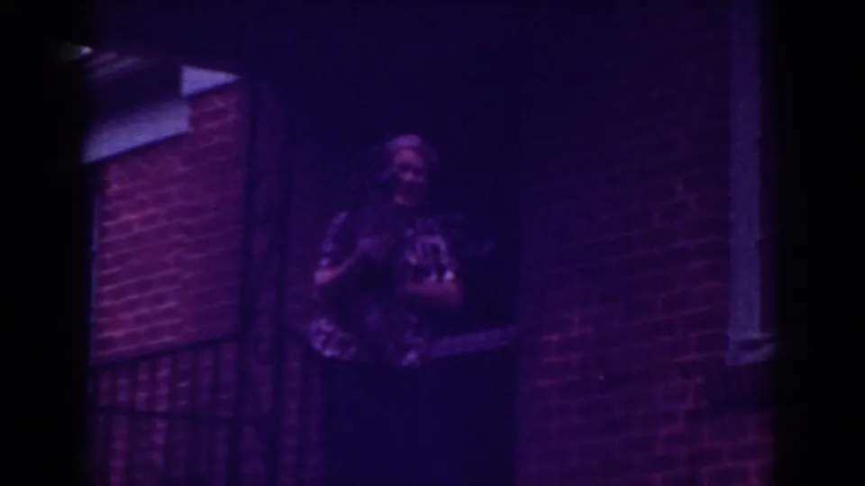 The woman turns toward the camera holding a small dog in front of the Raleigh brick residence.