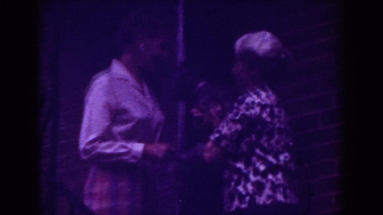 In Raleigh home-movie footage from 1962, two adult women stand near a brick front door during a small doorstep exchange.