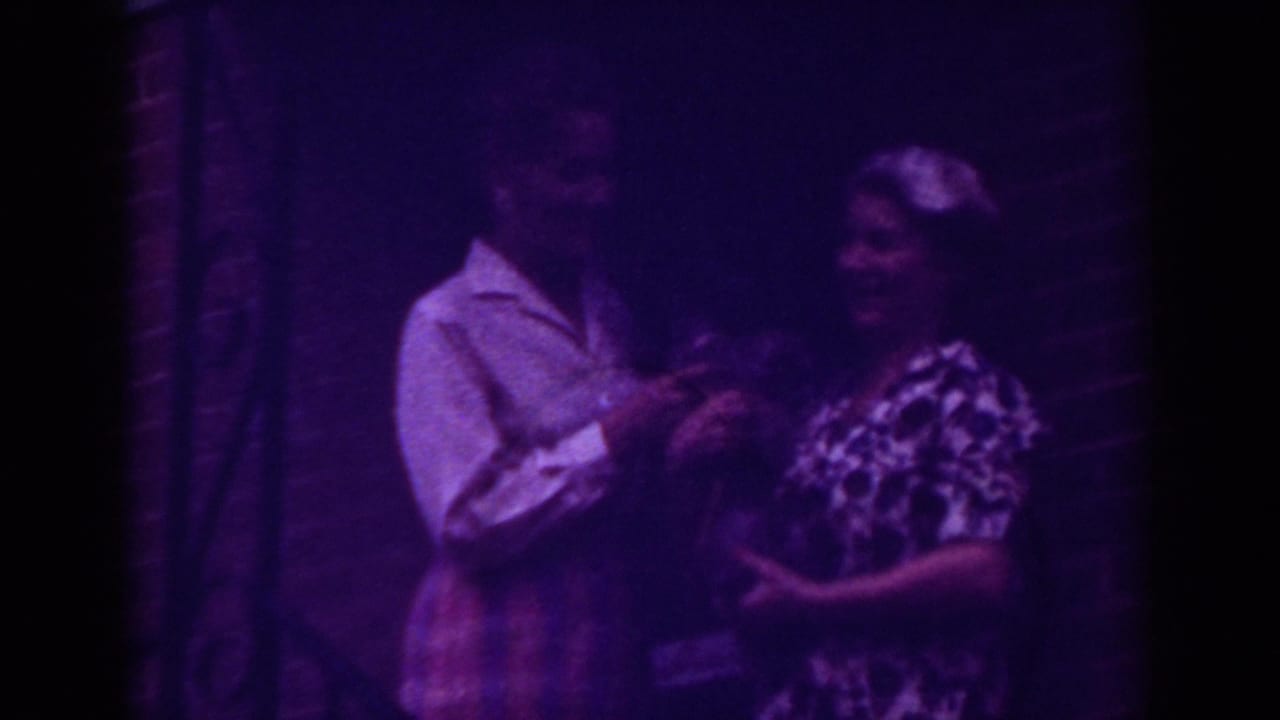 Two women face each other at a front door while handling a small dark object.