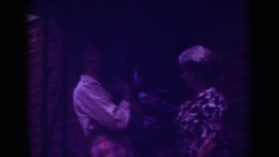 At the end of the clip, the two women remain by the Raleigh brick doorway, partly obscured by low light and the purple film cast.