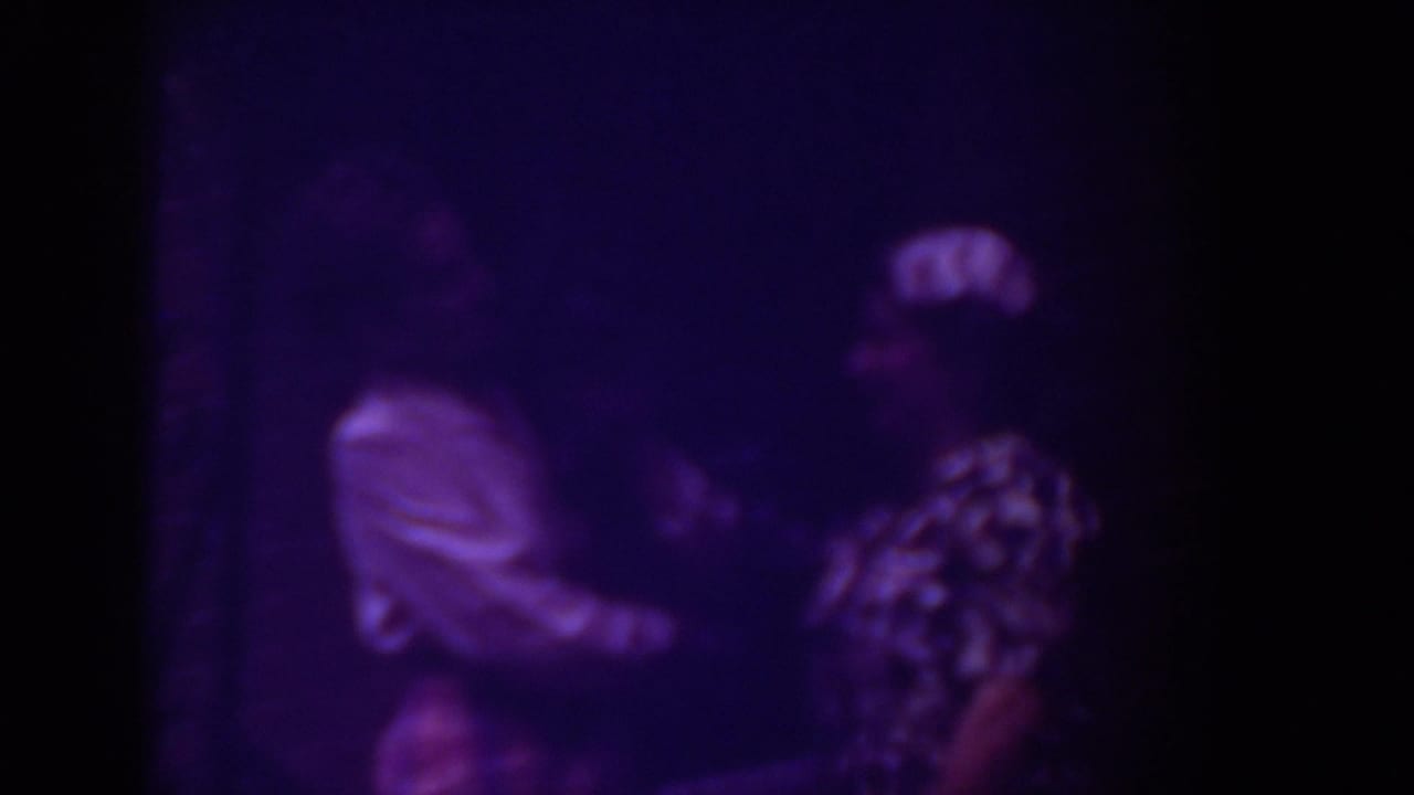 Purple-tinted 8mm frame from Raleigh, 1962, with two women facing each other in a dim outdoor or porch-like setting.