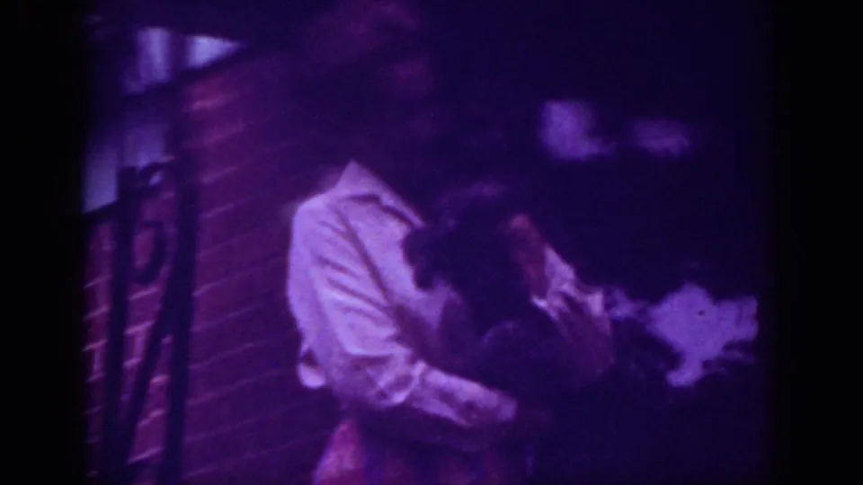 1962 Raleigh home-movie frame showing the woman leaning down toward the pet in a close affectionate gesture.