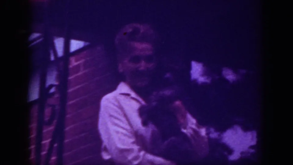 1962 Raleigh frame with a woman in a white collared shirt holding a dark pet near brickwork under dim light.