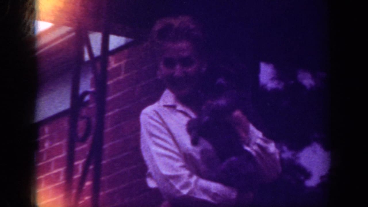 Woman in a light shirt holding a dark animal near a brick wall.