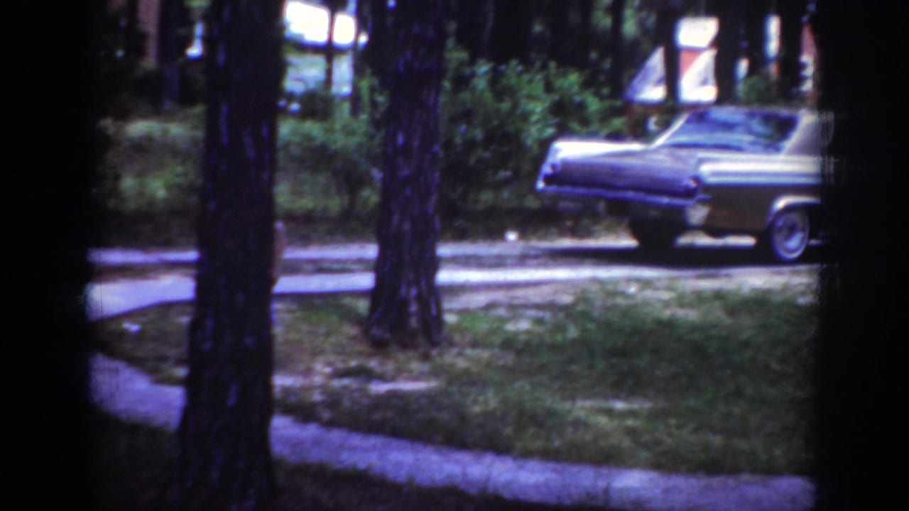 1962 Raleigh home-movie frame showing a chrome-trimmed sedan near a tree-lined residential lawn.