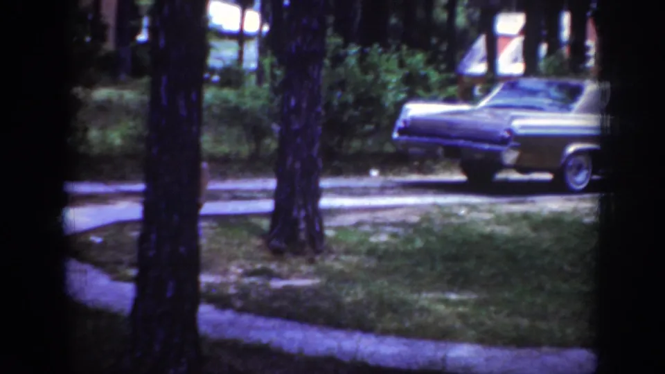 1962 Raleigh home-movie frame showing a chrome-trimmed sedan near a tree-lined residential lawn.