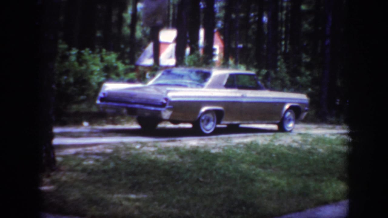 A mid-century sedan appears beside a pine-lined lawn in Raleigh, North Carolina, in 1962 home-movie footage.