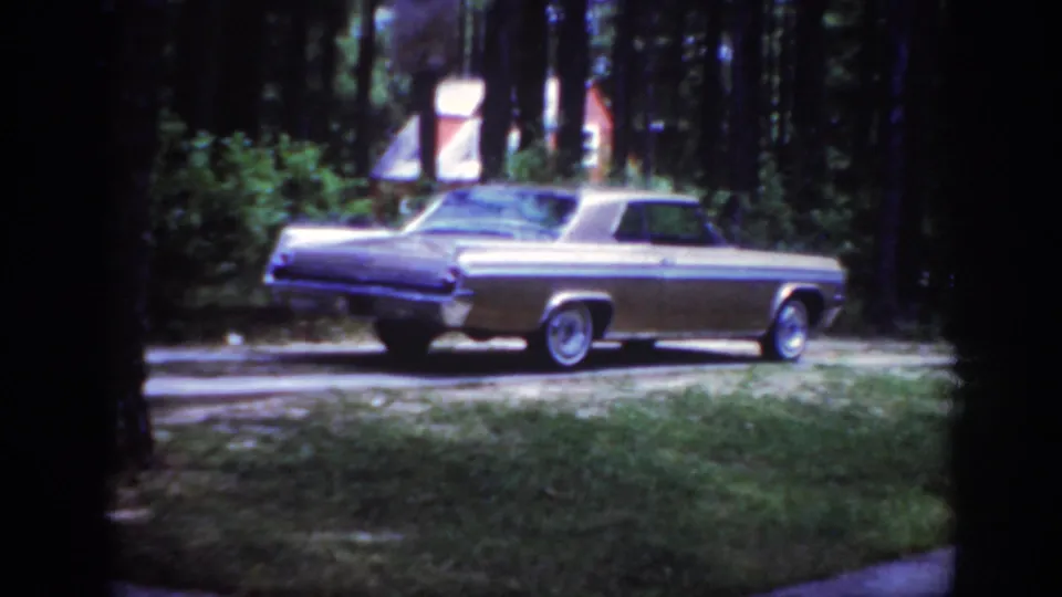 A mid-century sedan appears beside a pine-lined lawn in Raleigh, North Carolina, in 1962 home-movie footage.