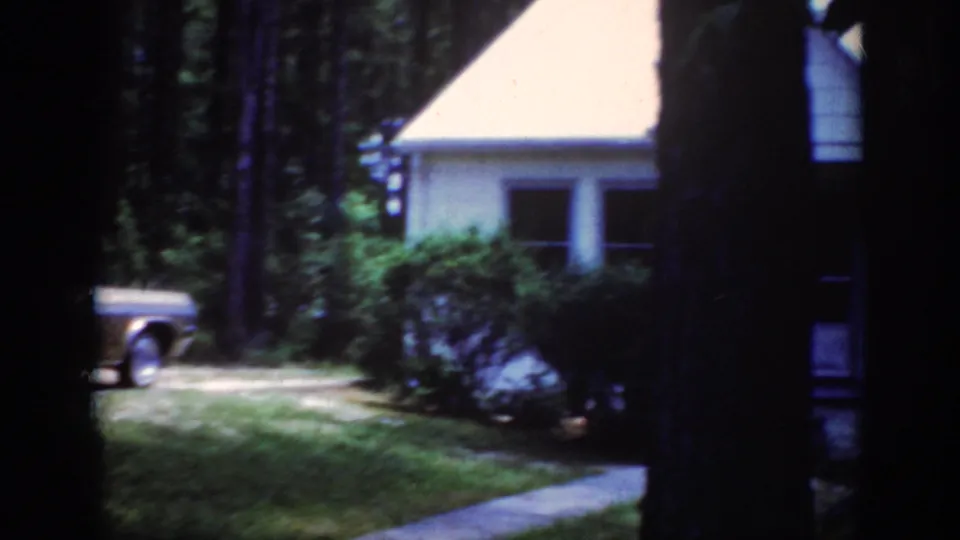 A partial view of the sedan passes near shrubs and a modest Raleigh house in 1962 8mm footage.