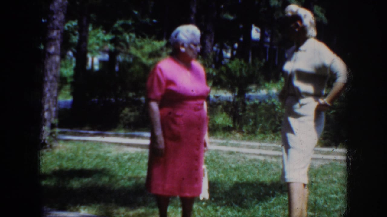 1962 Raleigh frame of two adult women in dresses standing outdoors among grass and trees, with one woman posed with a hand at her side.