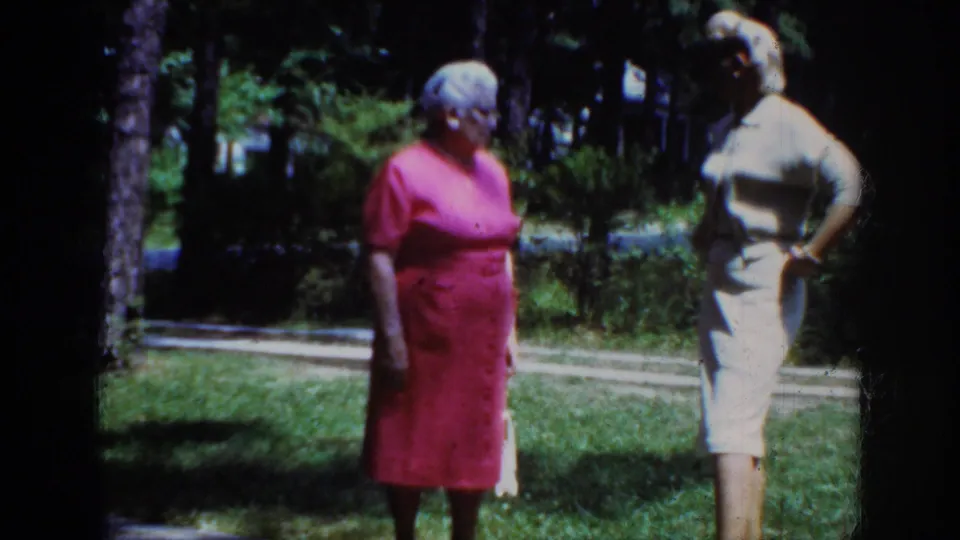 1962 Raleigh frame of two adult women in dresses standing outdoors among grass and trees, with one woman posed with a hand at her side.