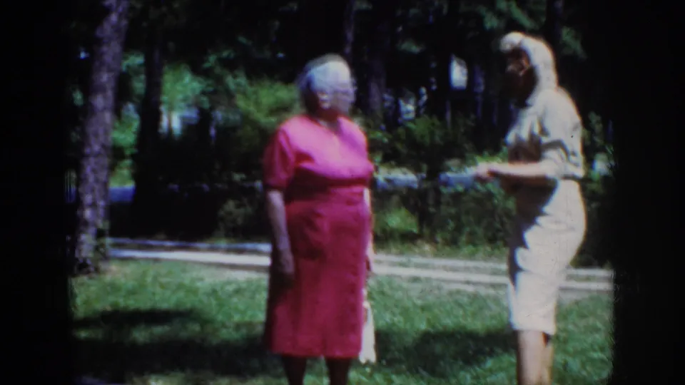 1962 Raleigh frame of two adult women outdoors, with the woman in a light dress appearing to gesture or adjust her outfit.
