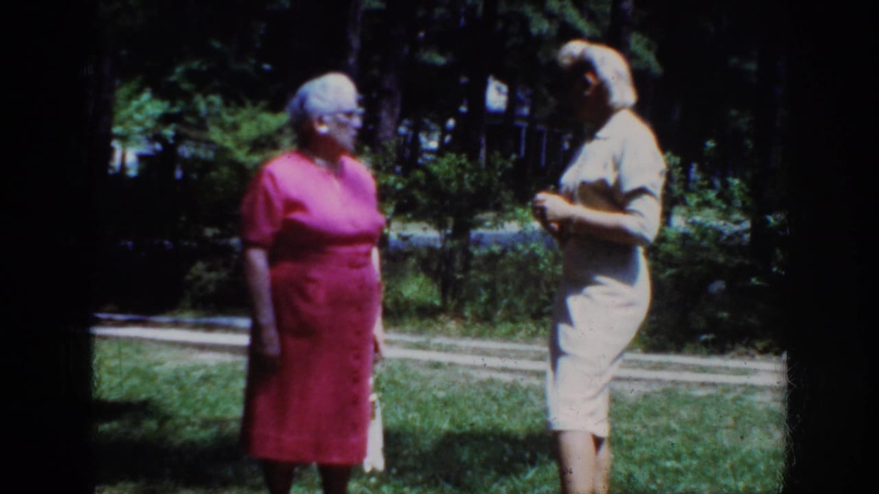 Two women remain on the lawn, one in a pink dress and one in a light dress.
