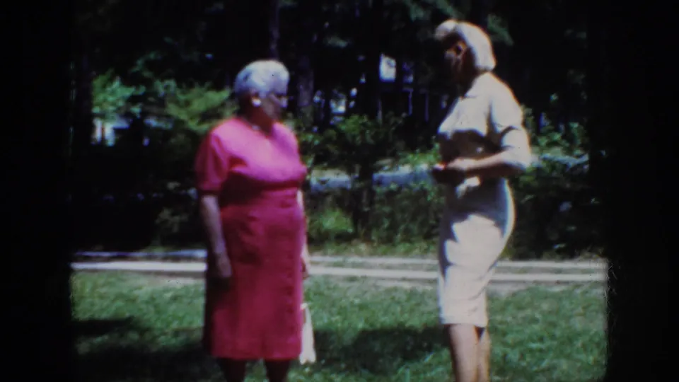 The home-movie frame shows the two women close together outdoors, with one gesturing slightly during the conversation.