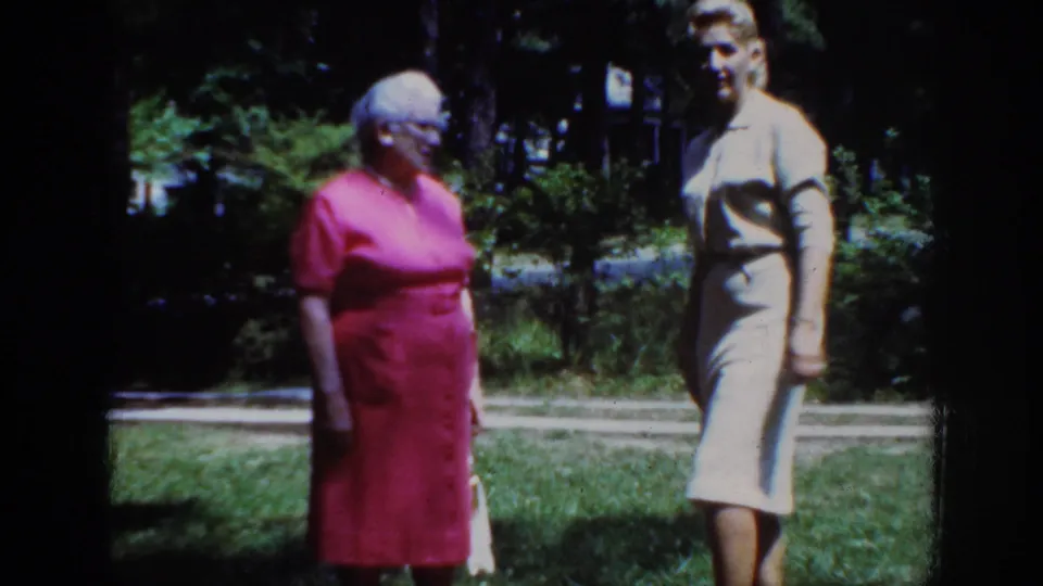 At the end of the clip, the woman in the light dress turns toward the camera while the woman in pink remains beside her.