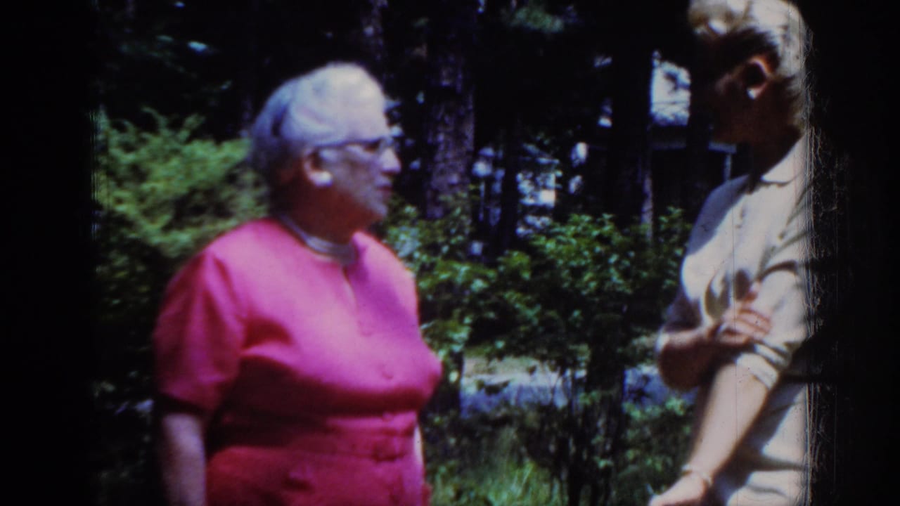 Older woman in a pink dress faces a younger woman in a light dress outdoors.