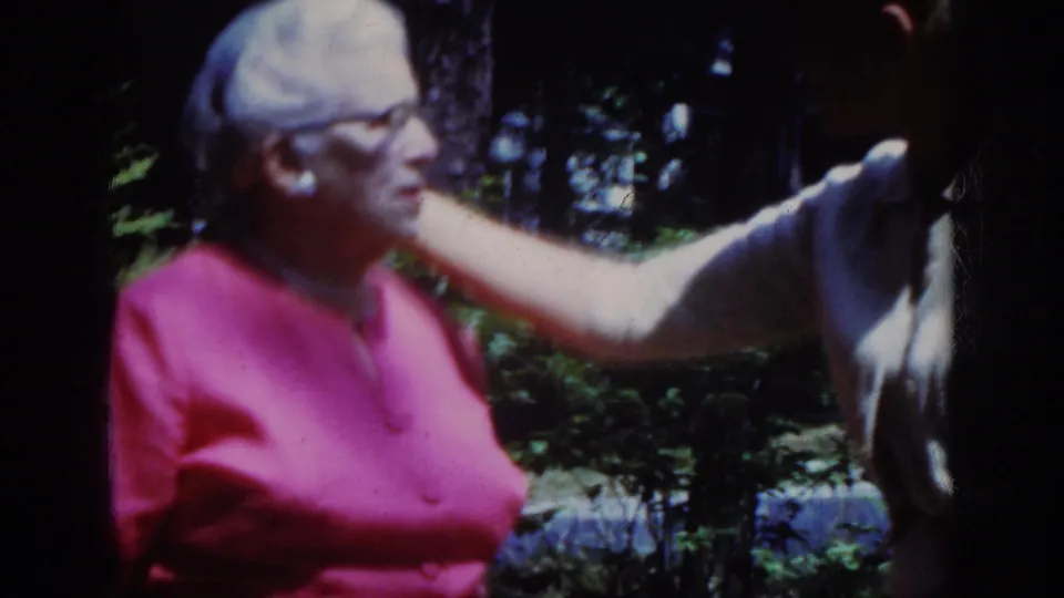 During the 1962 Raleigh home movie, the younger woman reaches gently toward the older woman's face in close conversation.
