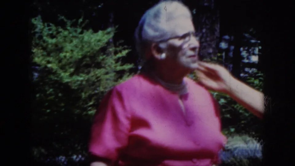 The older woman in pink and glasses smiles while a younger woman's hand touches her chin in the leafy Raleigh yard.