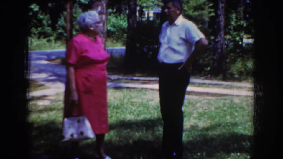 The final frame shows the elderly woman and man still facing each other in the garden-like outdoor setting in Raleigh.