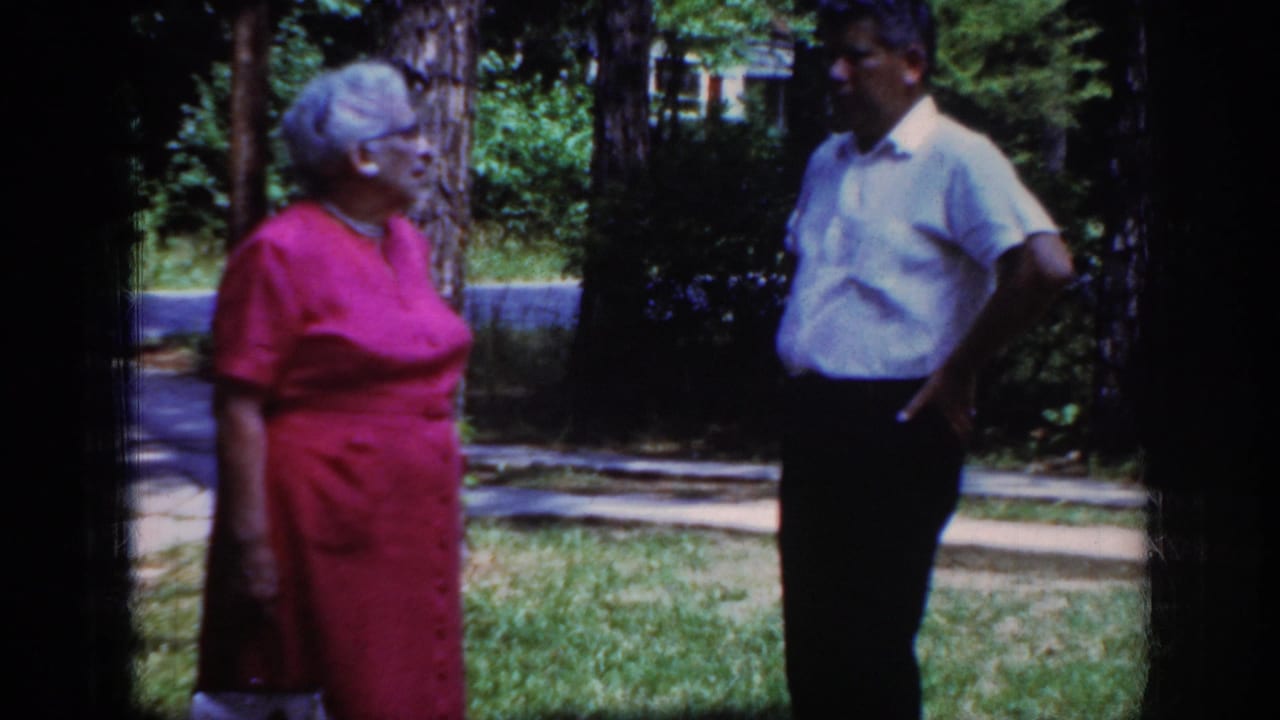 In Raleigh, North Carolina, 1962 home-movie footage, an older woman in a pink dress faces a man outdoors beside trees and grass.