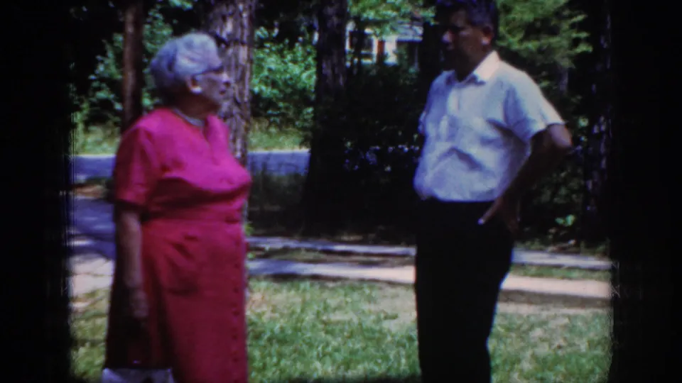 In Raleigh, North Carolina, 1962 home-movie footage, an older woman in a pink dress faces a man outdoors beside trees and grass.