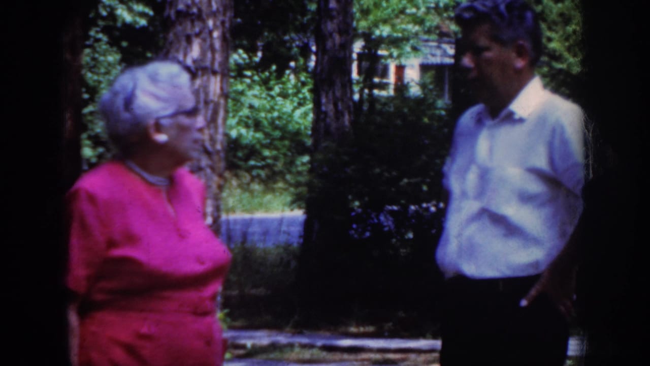 The 1962 Raleigh home-movie frame shows the woman in pink turned toward a man in a light button-up shirt outdoors.