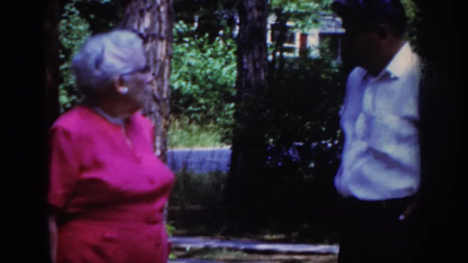 A Raleigh 1962 home-movie frame captures the woman in pink and the man in partial shade during their outdoor exchange.