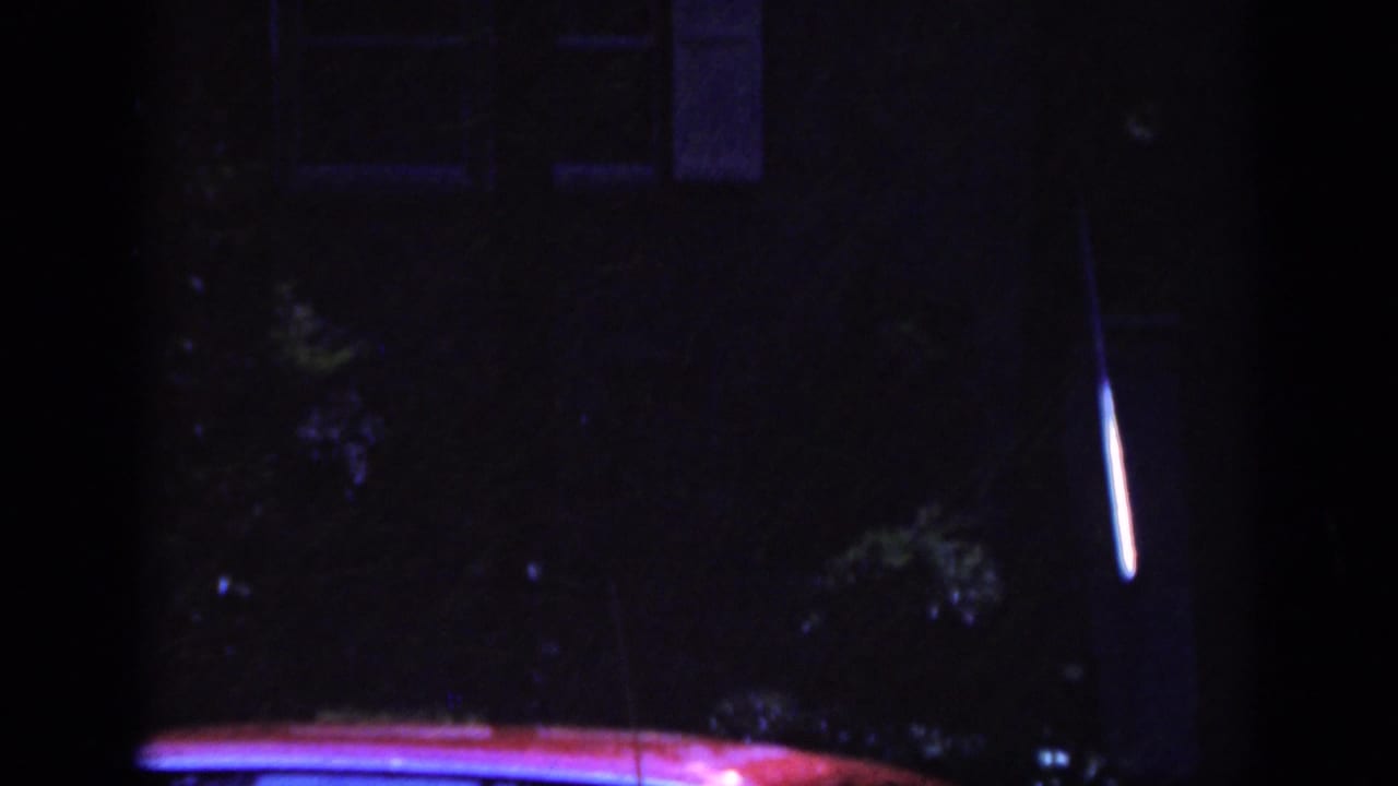 1962 Raleigh 8mm frame showing a dark residential scene with part of a red car reflecting blue and purple light.