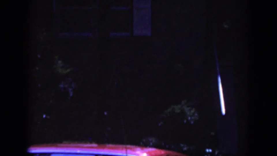 1962 Raleigh 8mm frame showing a dark residential scene with part of a red car reflecting blue and purple light.