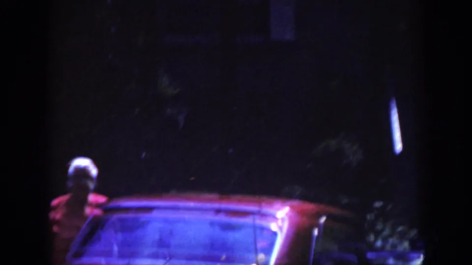 1962 Raleigh home-movie frame with an older woman beside a red car in a dark residential setting.