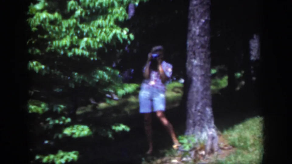 Closer 1962 Raleigh frame showing a woman filming from a grassy wooded area, with tree bark and foliage around her.