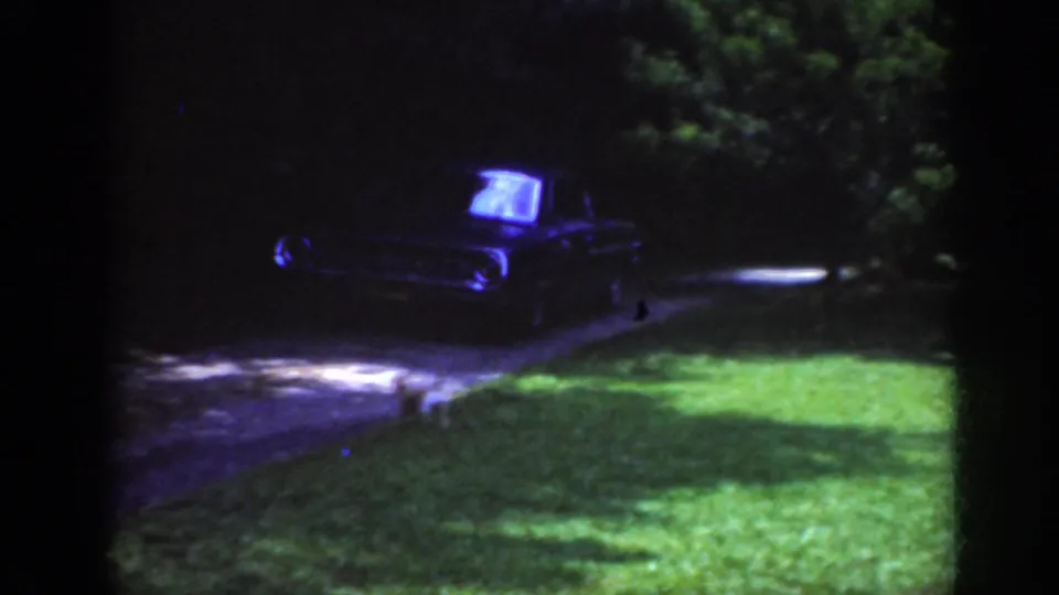 Raleigh 1962 home-movie frame showing a dark sedan on a driveway, partly obscured by night exposure and trees.