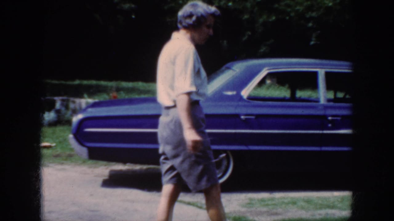 Older woman walks in profile past the rear side of a blue sedan.