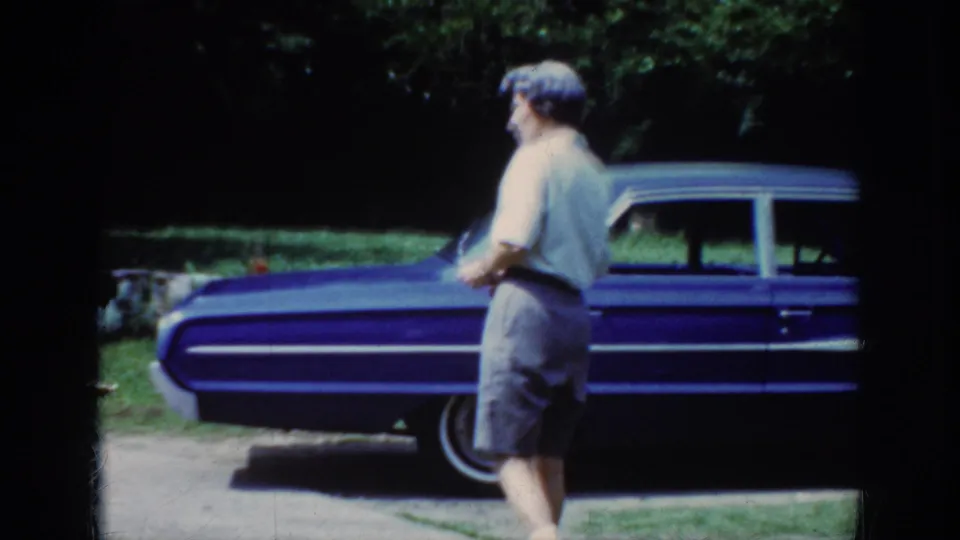 The woman appears near the blue sedan holding eyeglasses, framed by dark 8mm borders with lawn and trees behind.
