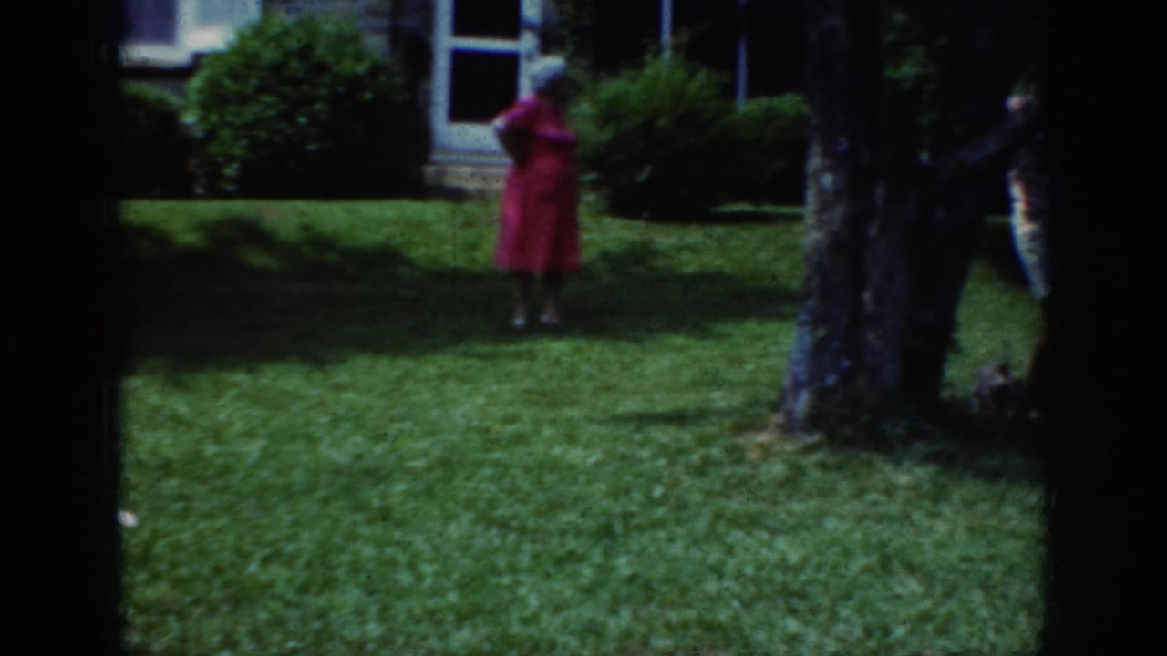 The same woman appears farther back on the lawn, framed by tree trunks with a house and shrubbery behind her.