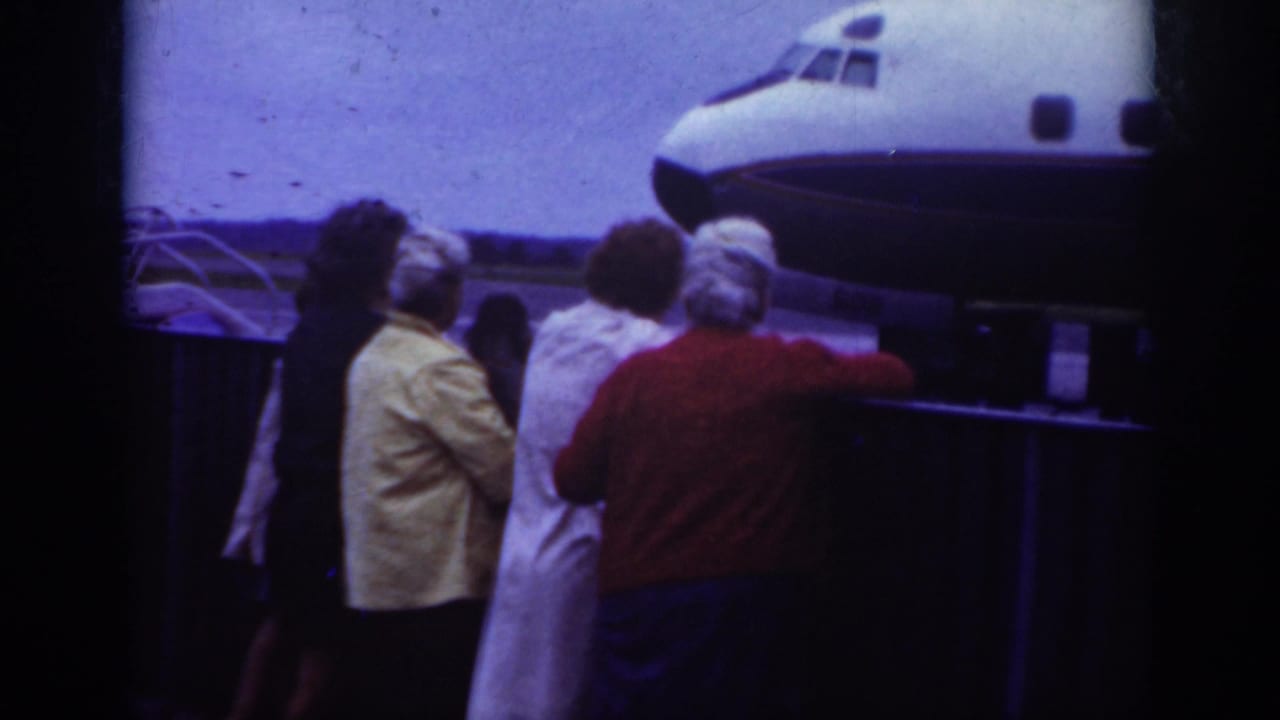 In Raleigh, 1962, a small crowd in period clothing watches near the nose of a commercial airliner on the airport tarmac.