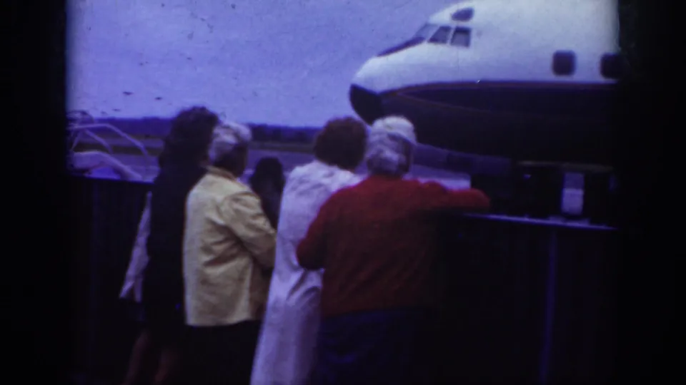 In Raleigh, 1962, a small crowd in period clothing watches near the nose of a commercial airliner on the airport tarmac.