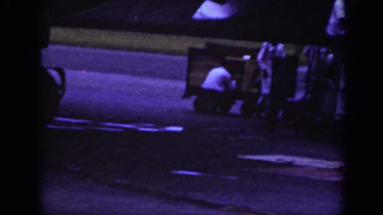Raleigh 1962 airport ground scene with a worker crouched beside cargo equipment and a baggage cart under low night light.