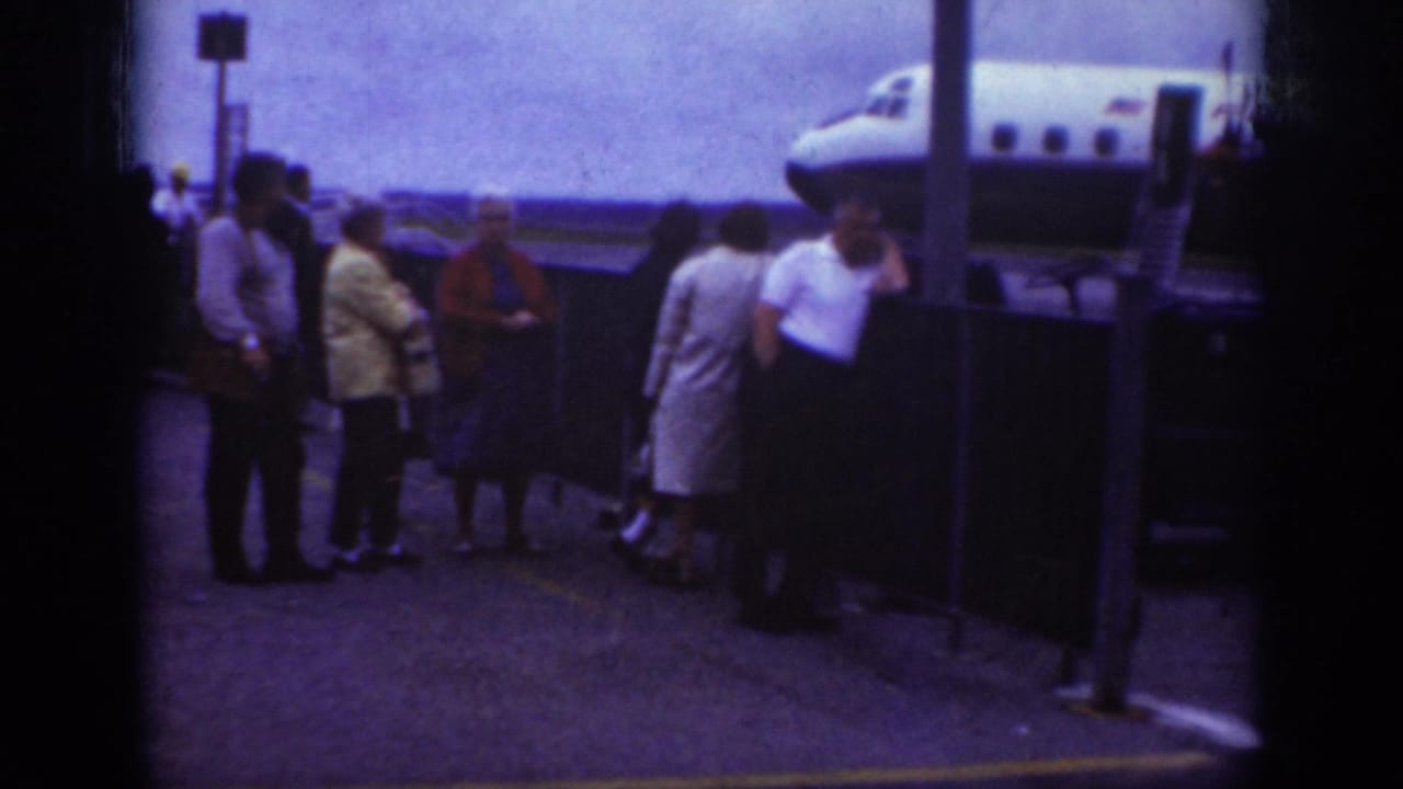 1962 Raleigh airport frame with adults gathered at a tarmac railing while an Eastern Airlines aircraft nose is visible nearby.