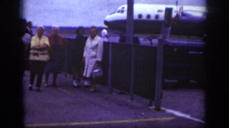 Passengers in early 1960s coats and suits walk together on the Raleigh airport ramp beside the Western Airlines aircraft and service vehicle.