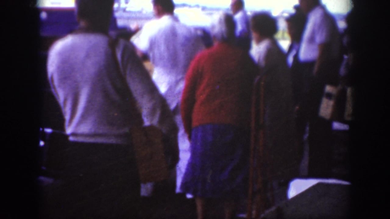 Travelers seen from behind gathering near an aircraft boarding area on the tarmac.
