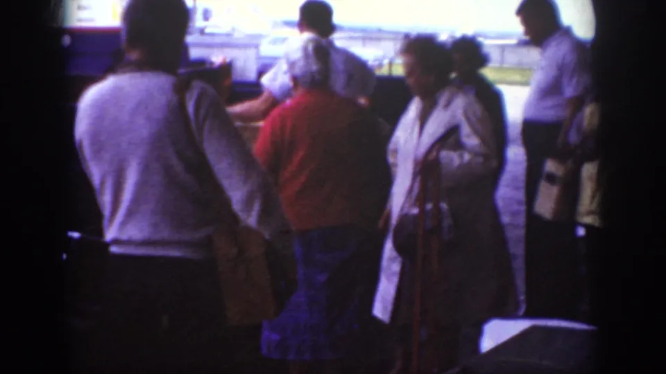 1962 Raleigh tarmac scene with passengers in period clothing waiting near an aircraft, captured with grainy purple-tinted 8mm texture.