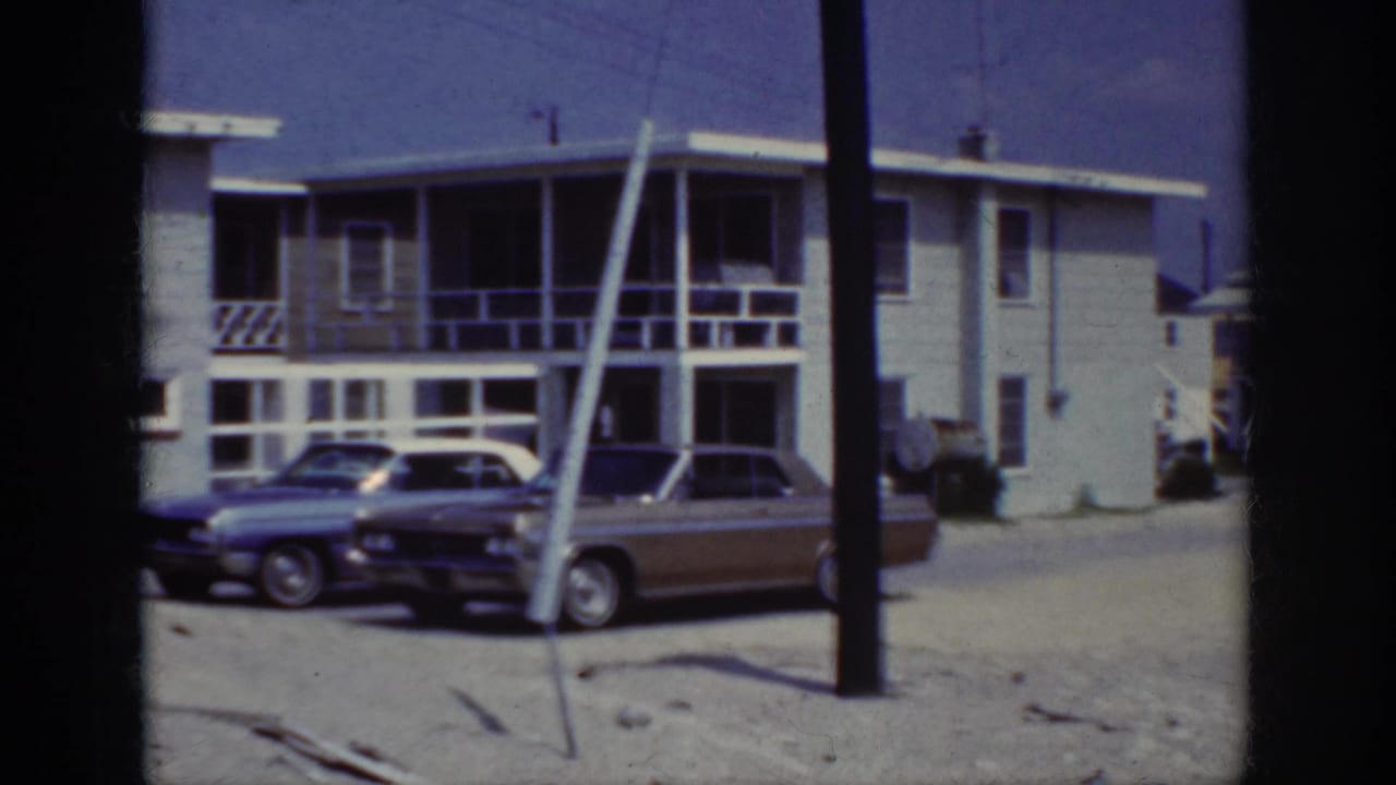 Blue convertible and brown sedan parked near white-railed houses with a utility pole in the foreground.