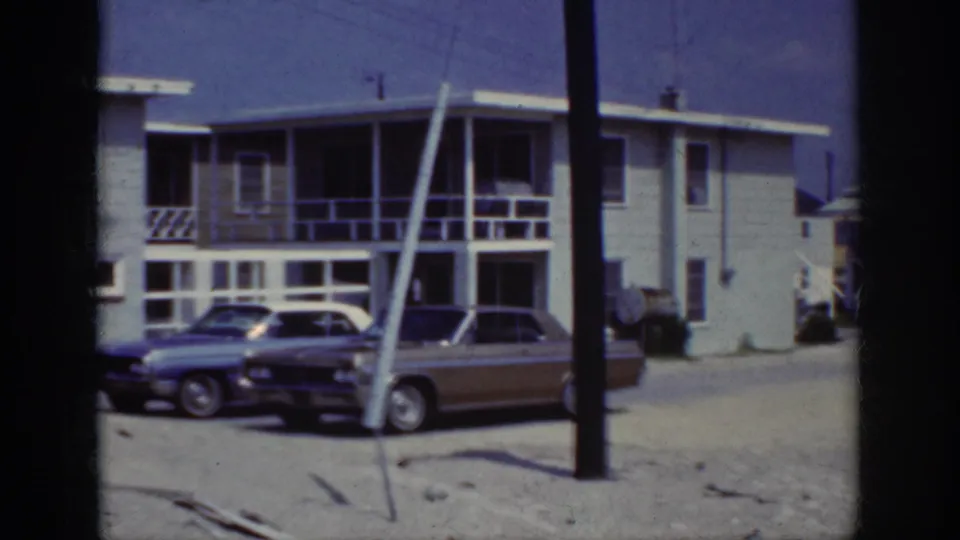 Parked classic cars and residential balconies appear in this 1962 Raleigh home-movie frame, partly blocked by a pole.