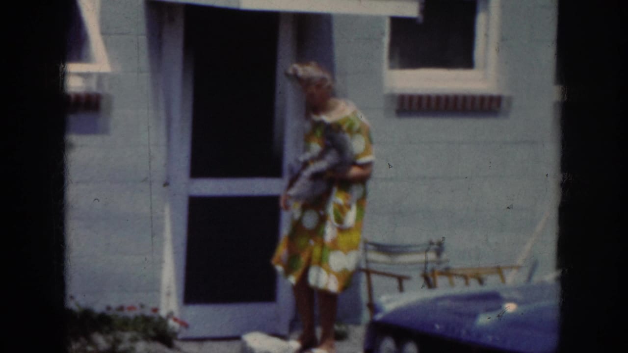 In 1962 Raleigh home-movie footage, a woman in a patterned dress holds a small dog near a screen door and porch chair.
